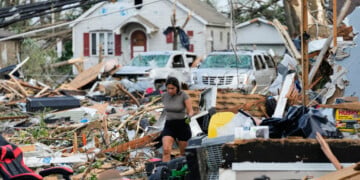 A woman walks among debris after a tornado struck Monday, July 27, 2026, in Menasha, Wis. (AP Photo/Kayla Wolf)