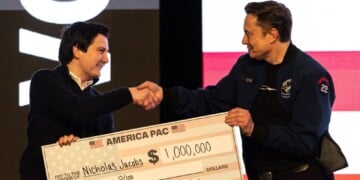 FILE - Elon Musk hands over a million dollar check to Nicholas Jacobs during a town hall in Green Bay, Wis., March 30, 2025. (AP Photo/Jeffrey Phelps, File)